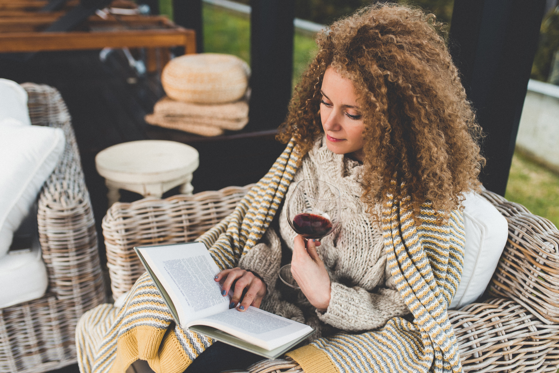 woman-reading-a-book-in-an-armchair-at-home-with-a-glass-of-wine