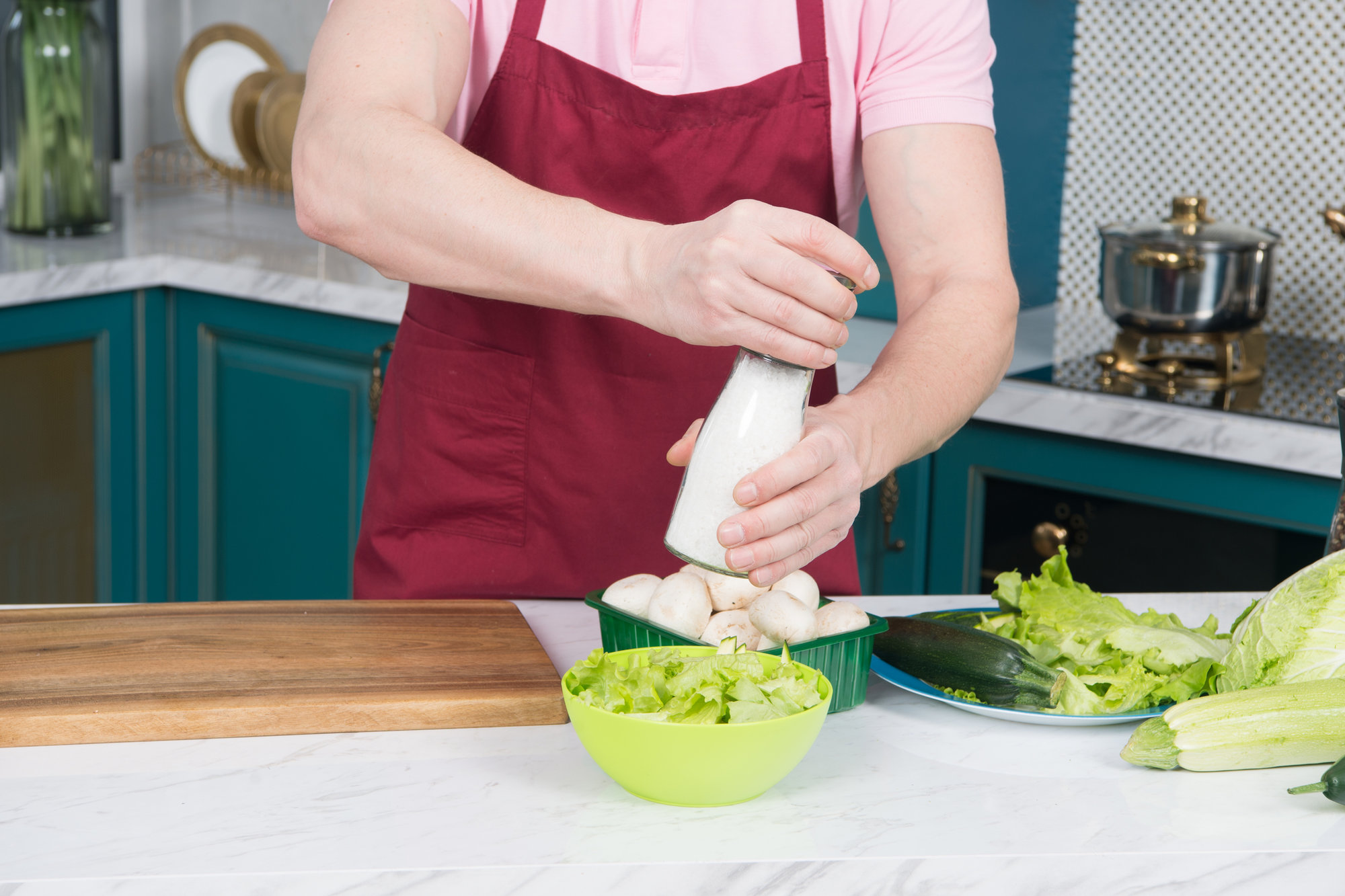 Male chef salting vegetable salad. Cook adding salt to salad with mushrooms and paprika. Man at kitchen preparing dinner