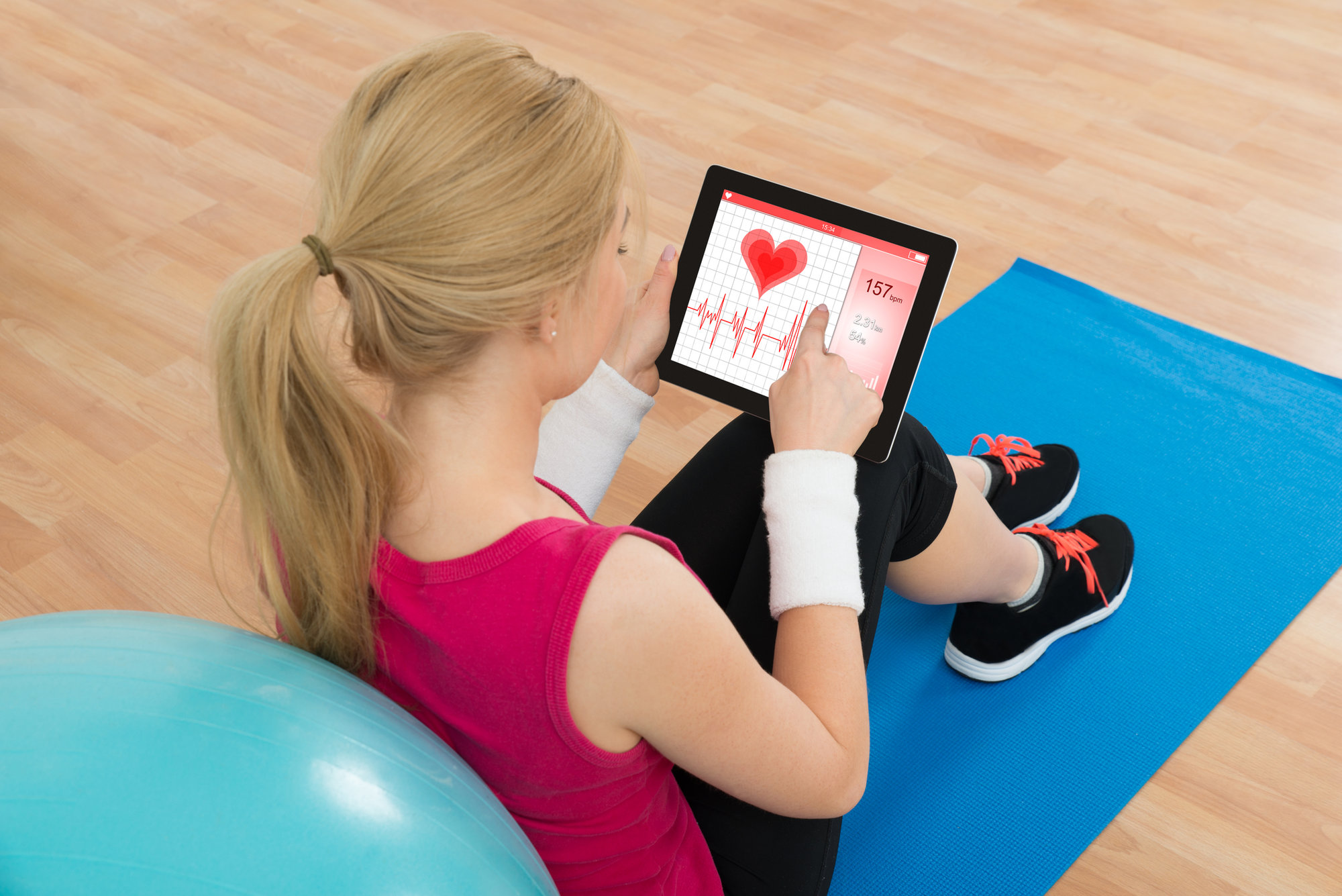 Young Woman Looking At Heart Pulse Rate On Digital Tablet In Living Room