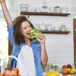 Young woman in the kitchen preparing food and singing into broccoli