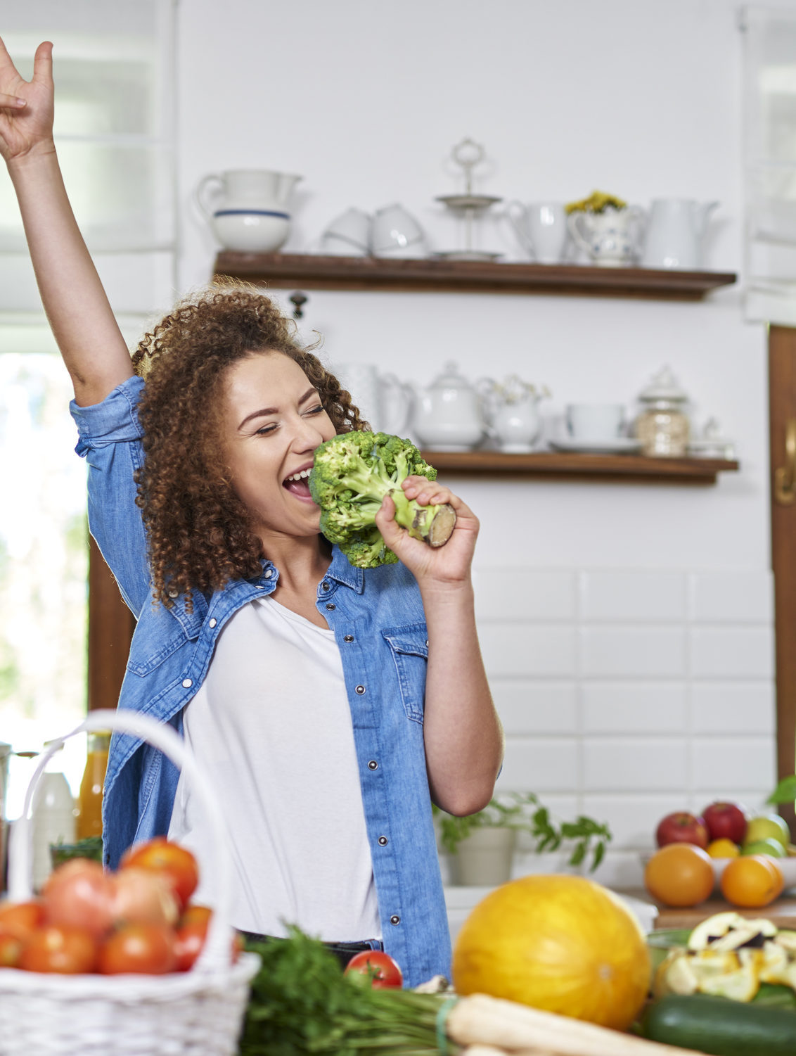 Young woman in the kitchen preparing food and singing into broccoli