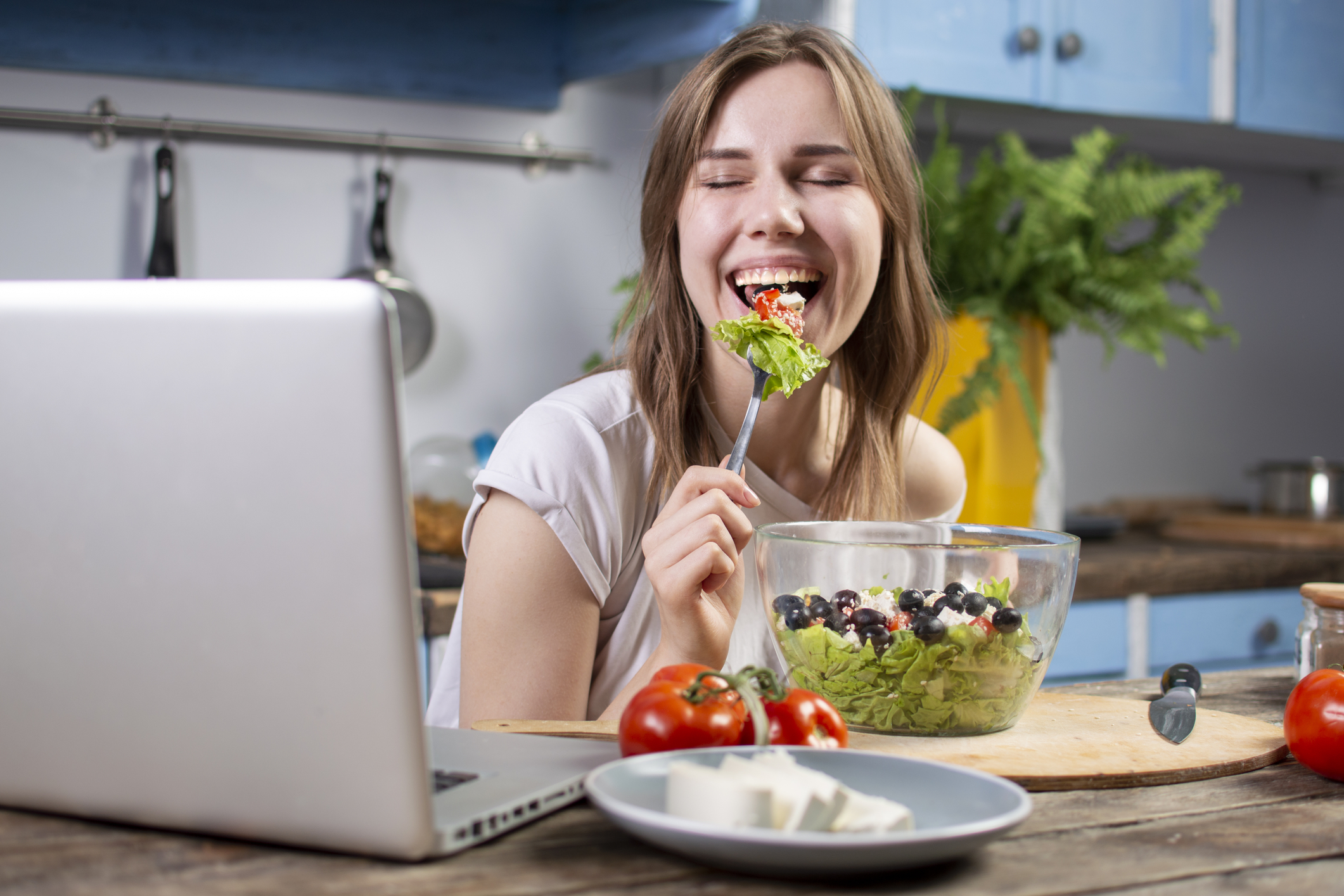 young woman eating a salad in front of laptop in kitchen