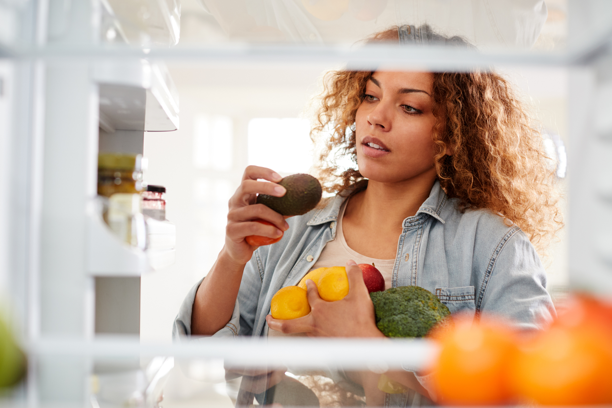 View Looking Out From Inside Of Refrigerator As Woman Opens Door And Packs Food Onto Shelves