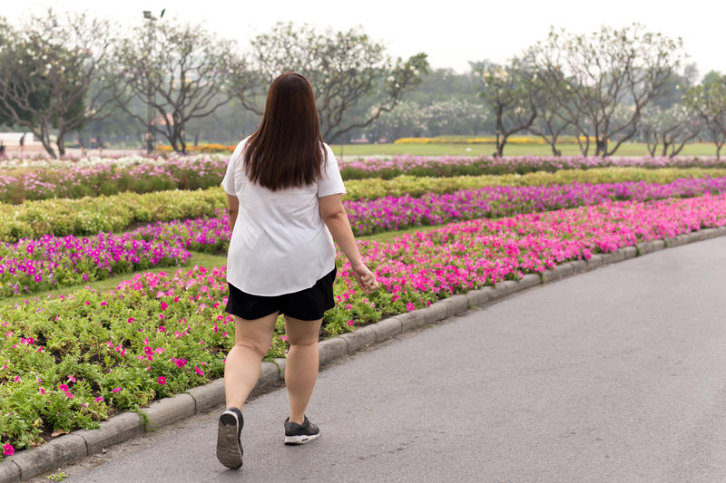 Health care concept overweight woman walking in the park with colorful flower