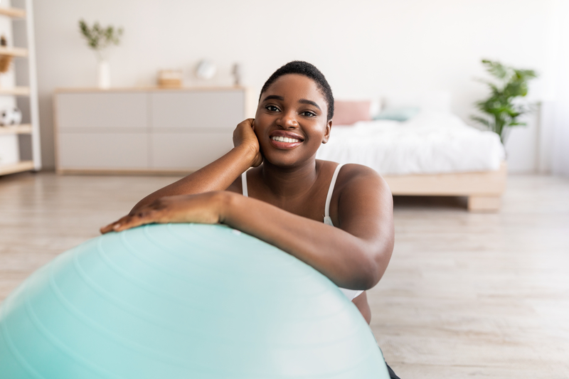 black woman sitting near fitness ball, smiling at camera indoors