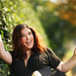 Happy woman outside in front of a wall of leaves