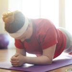 woman working out on yoga mat in sunlit fitness studio: holding plank exercise